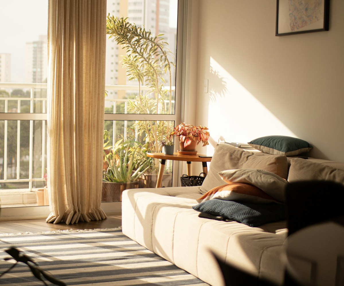 A sunlit living room opening through sliding doors onto a planted balcony