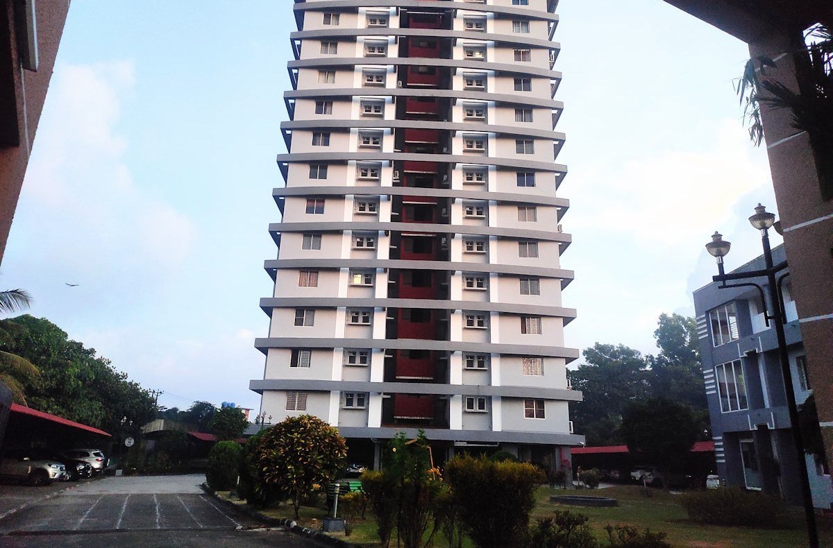 A single residential tower with stepped balcony bands seen from its driveway