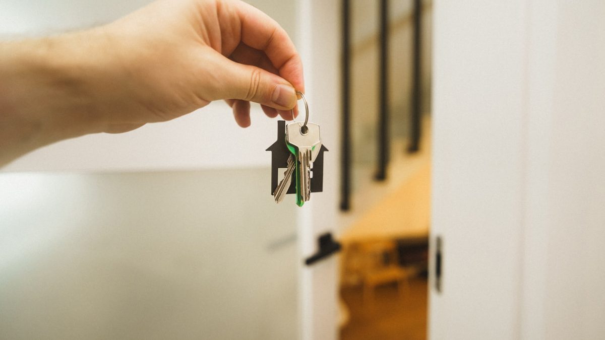 A hand holding a set of keys with a house shaped fob in front of an open door