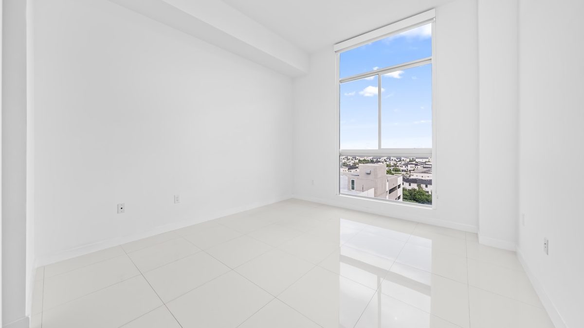An empty, newly finished apartment room with a window onto low rise rooftops
